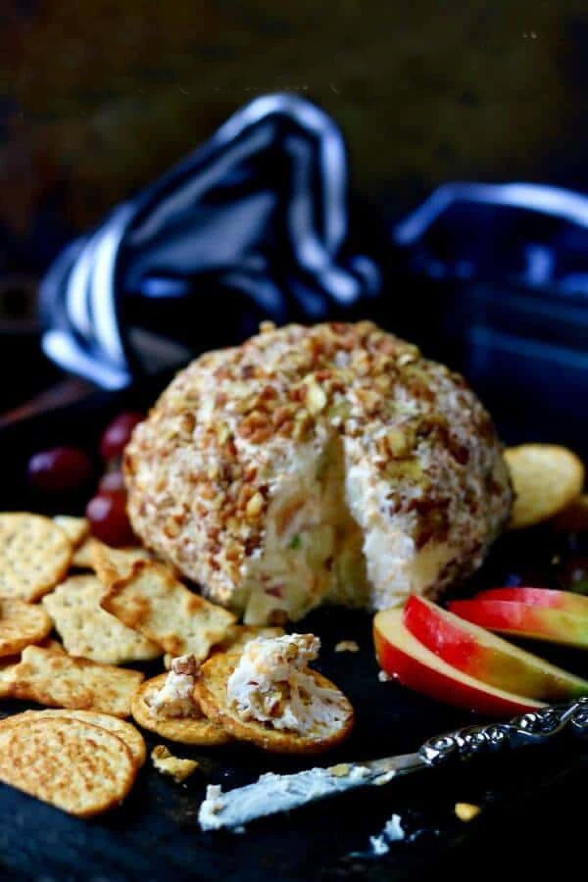 Cheeseball covered in pecans with crackers and apple slices.