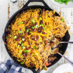 An iron skillet filled with pasta and topped with bacon and green onions.