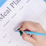 A woman writing down the weekly meal plan with a text overlay for Pinterest.