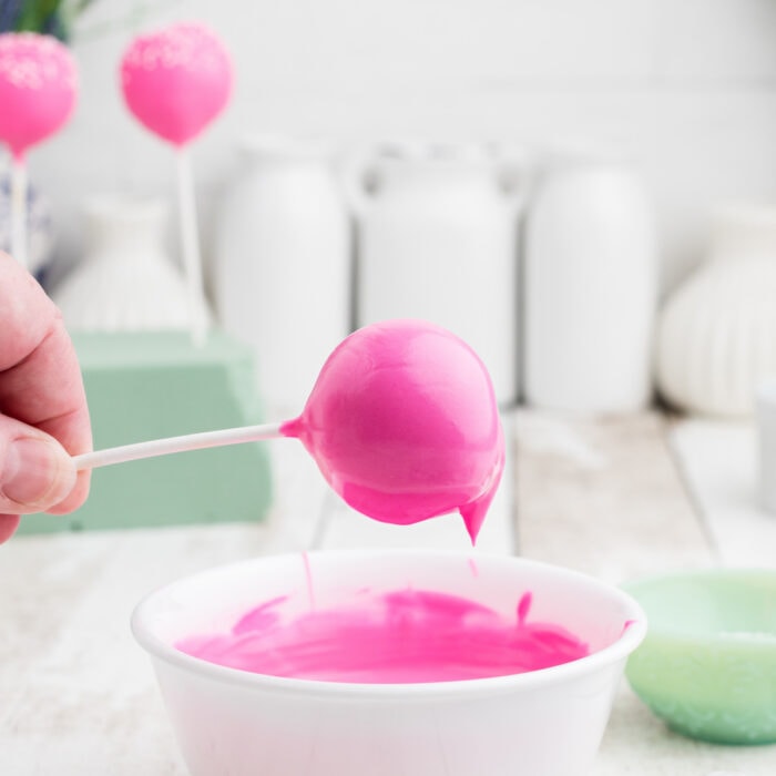 A pink cake pop being dipped in melted pink candy melt.