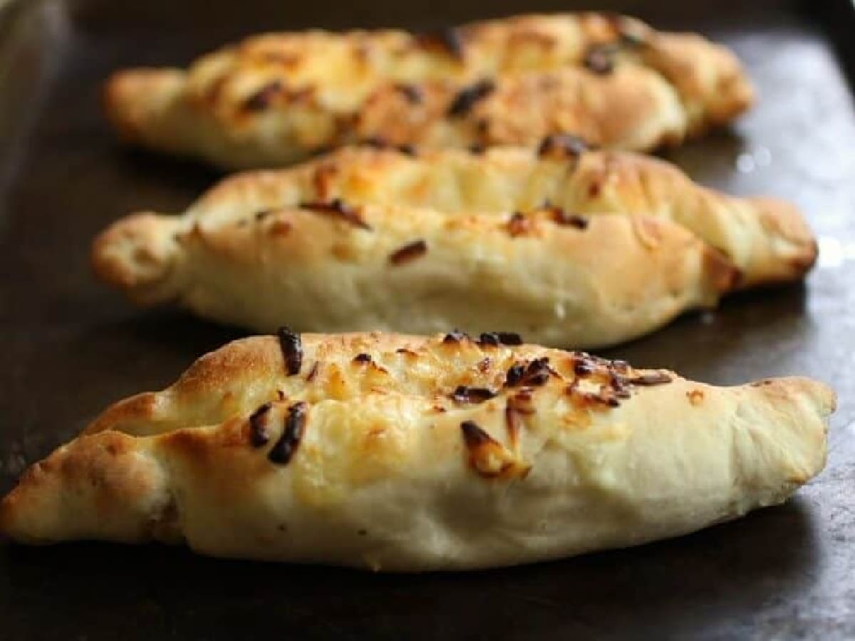 Golden brown Khachapuri with flecks of caramelized onions on top and cheese oozing out the sides.