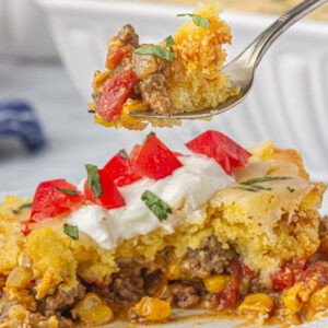 Closeup of Jiffy Mexican cornbread casserole on a plate with a fork lifting a bite.