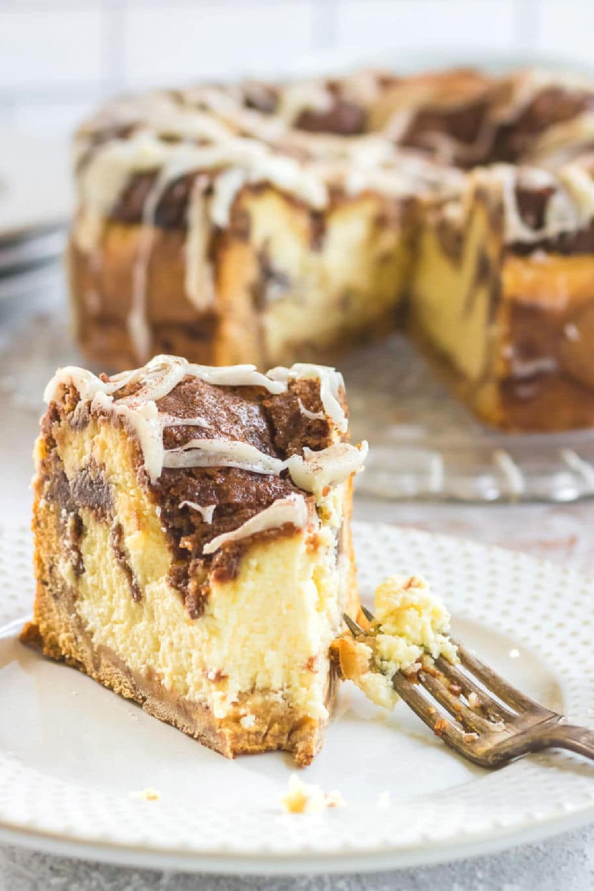 A slice of cheesecake with a cinnamon crumble topping is on a plate in front of the whole cheesecake.