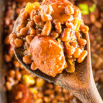 A ladle full of sliced kielbasa and saucy baked beans is being served. Title text overlay for Pinterest.