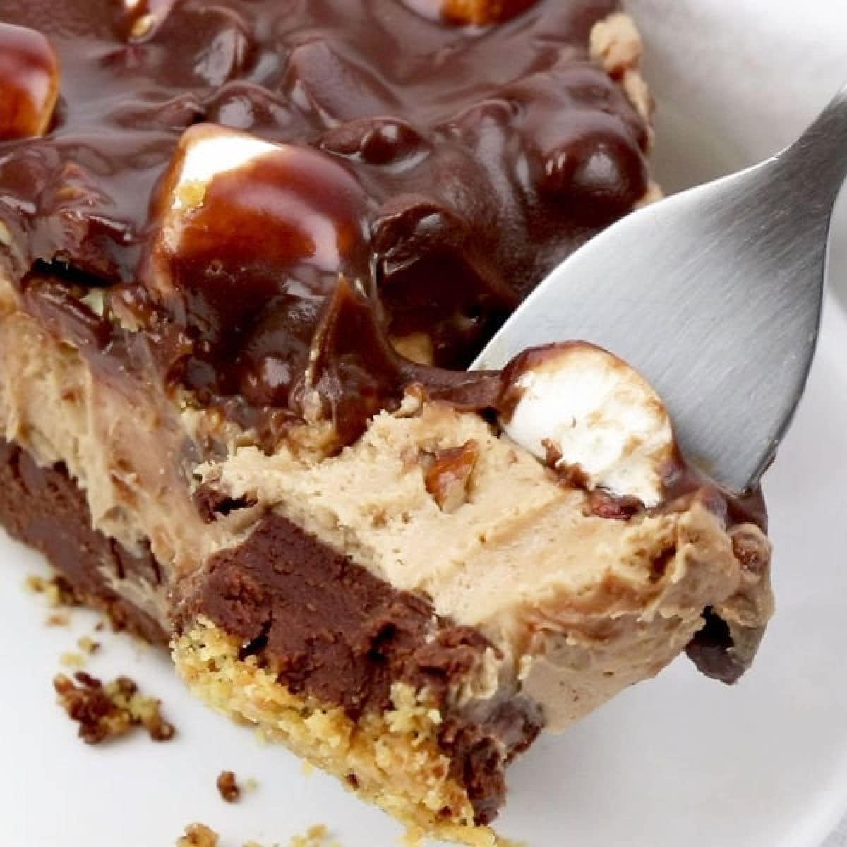 A super closeup of the pie showing layers of graham cracker crust, chocolate ganache, peanut butter mousse, and pecans and marshmallows covered in more chocolate.