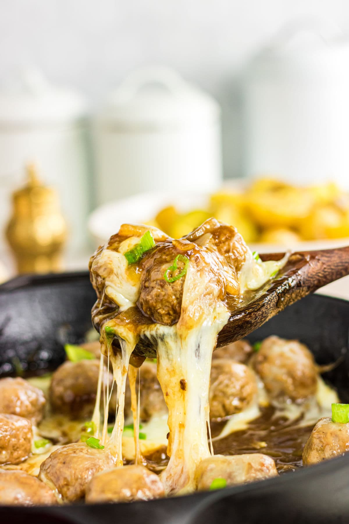 A wooden spoon removing the meatballs from the skillet with gooey cheese hanging off the spoon.