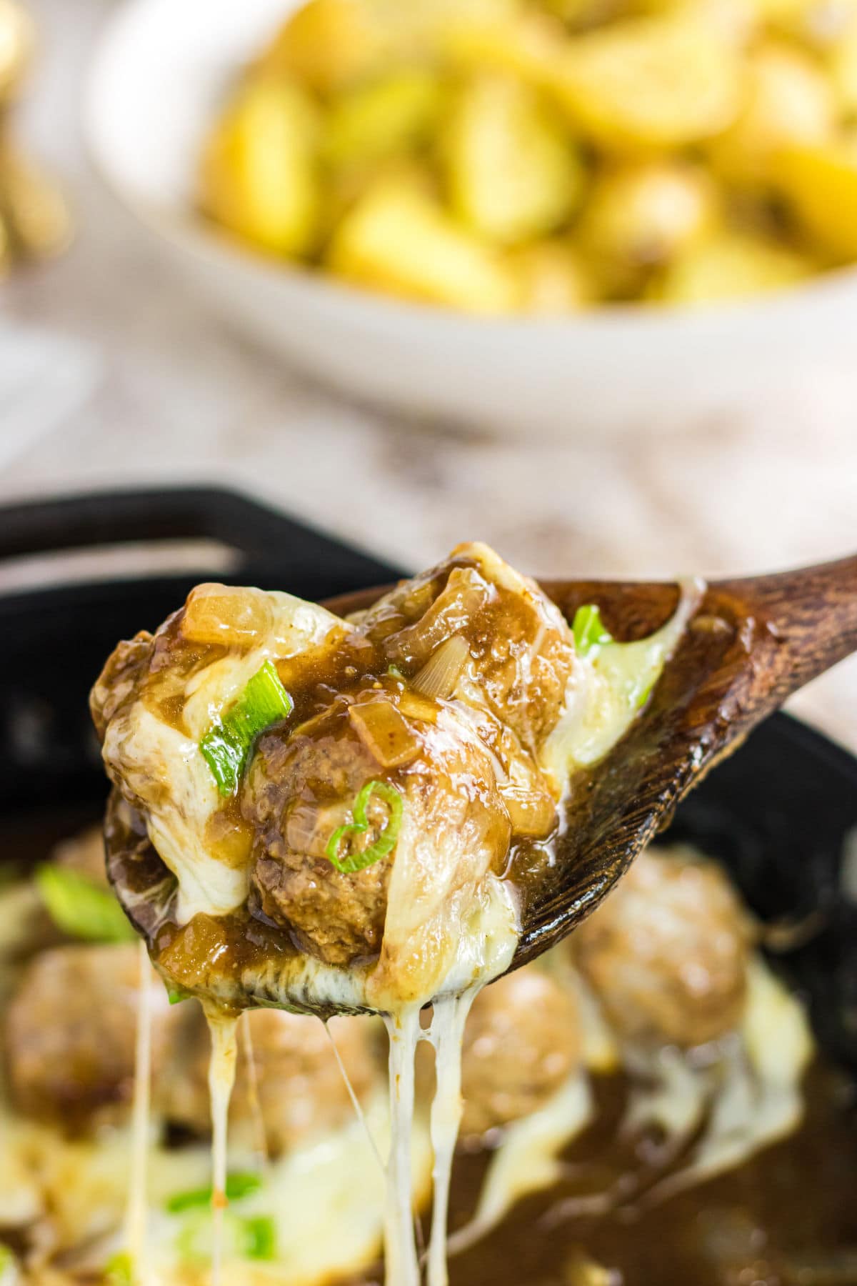 Closeup of meatballs being spooned out of the skillet with gooey cheese covering the meatballs and spoon.