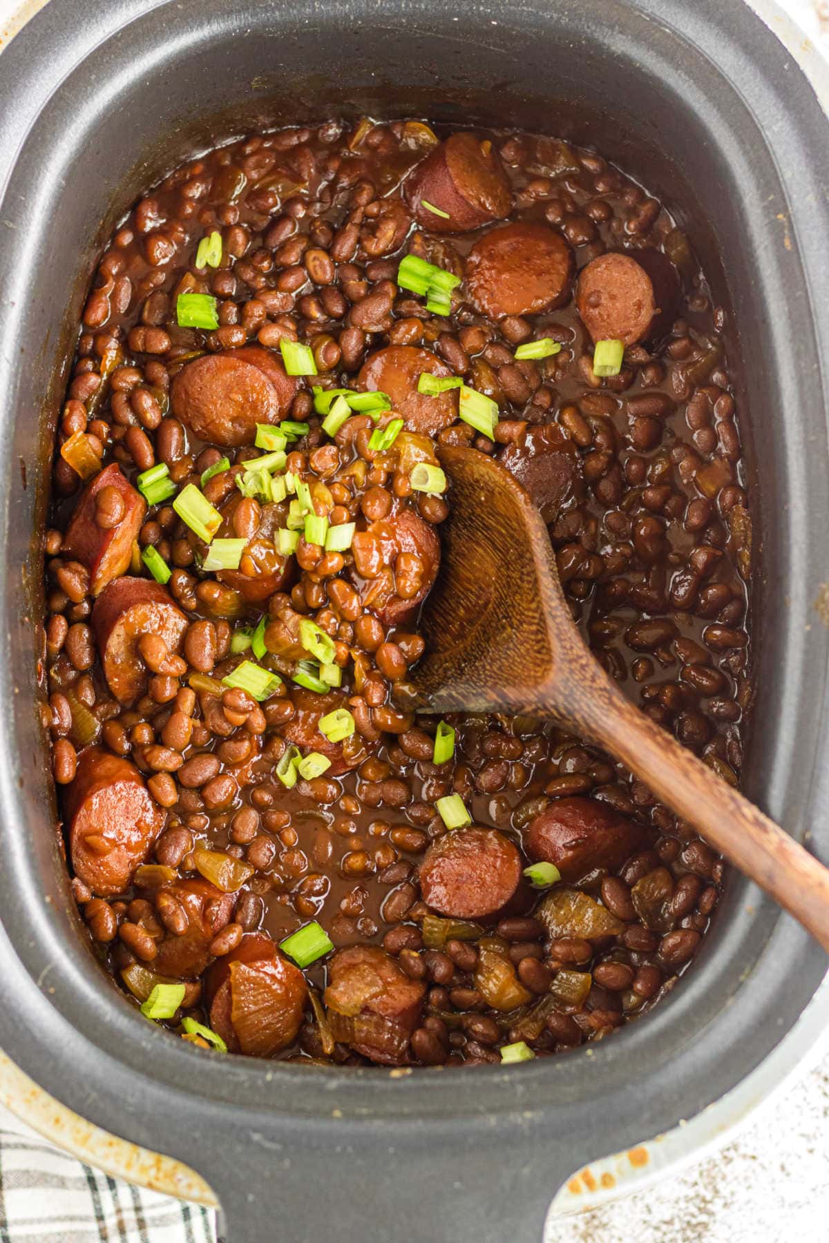 Overhead view of a crockpot with finished kielbasa and baked beans in it.