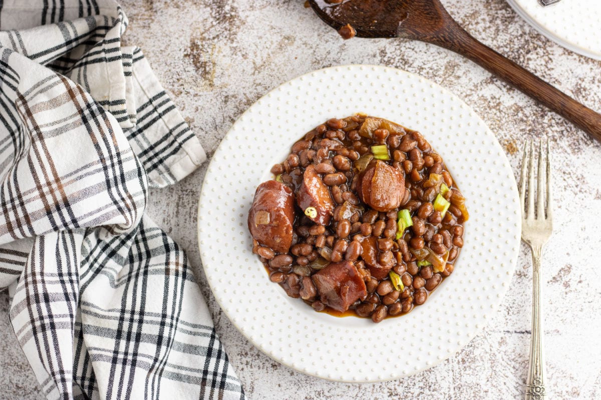 A white plate filled with baked beans and kielbasa.