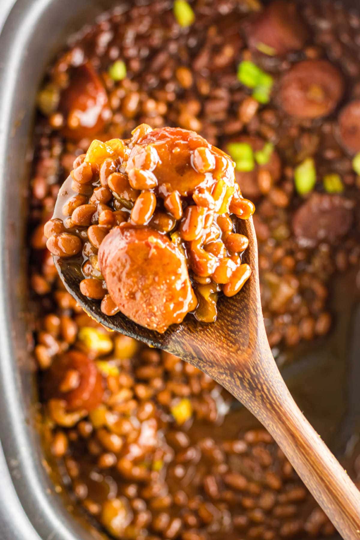 A serving spoon with filled with baked beans and kielbasa sausage.