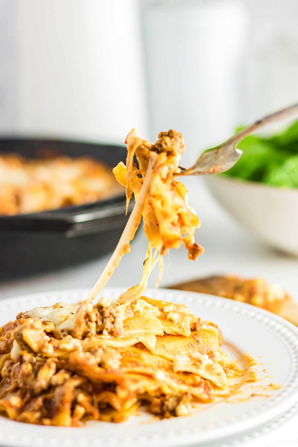 A serving of lasagna on a plate with a fork lifting a bite away.