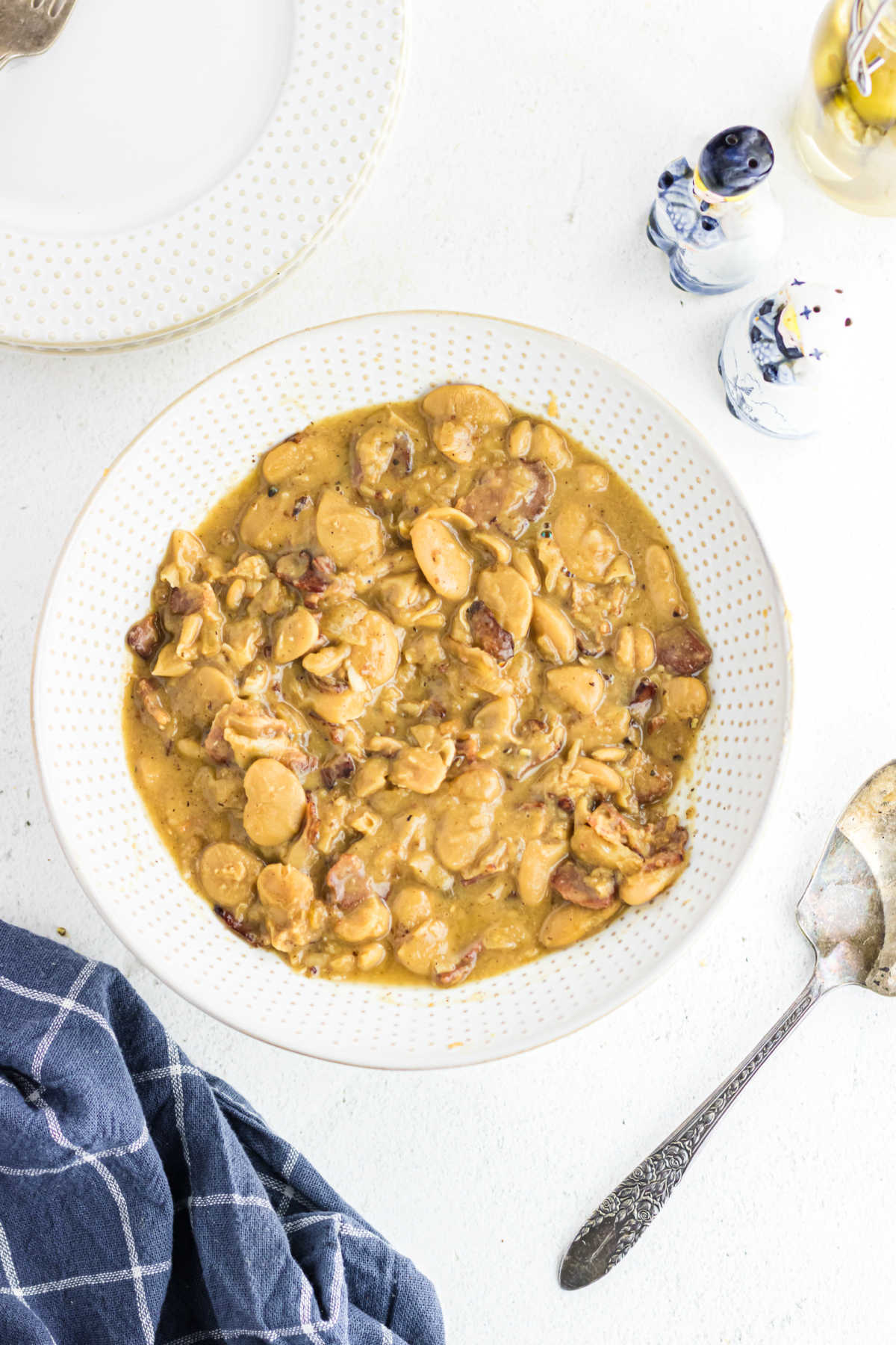 A bowl of butter beans with onions and bacon on a white table.