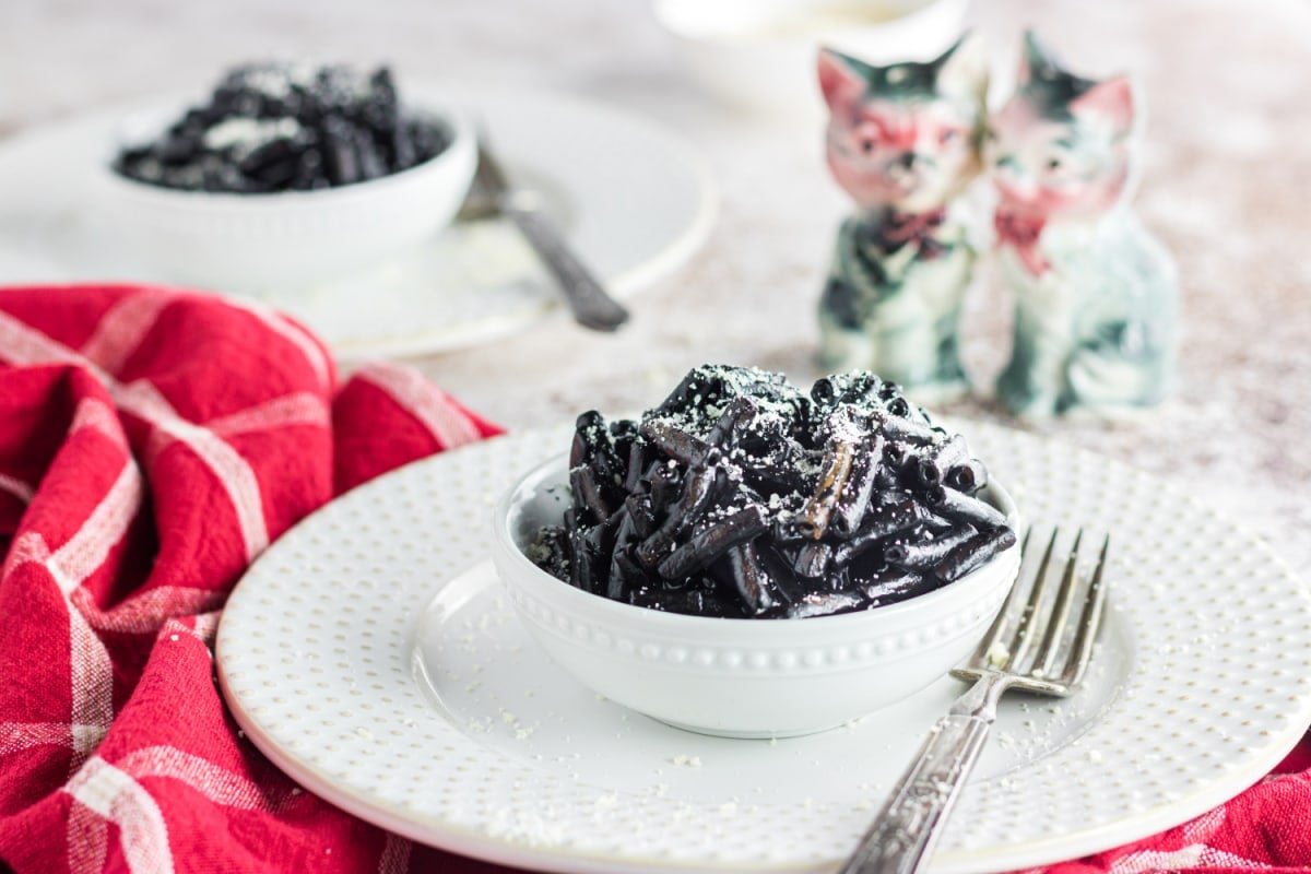 A Halloween table set with spooky black mac and cheese in white bowls.