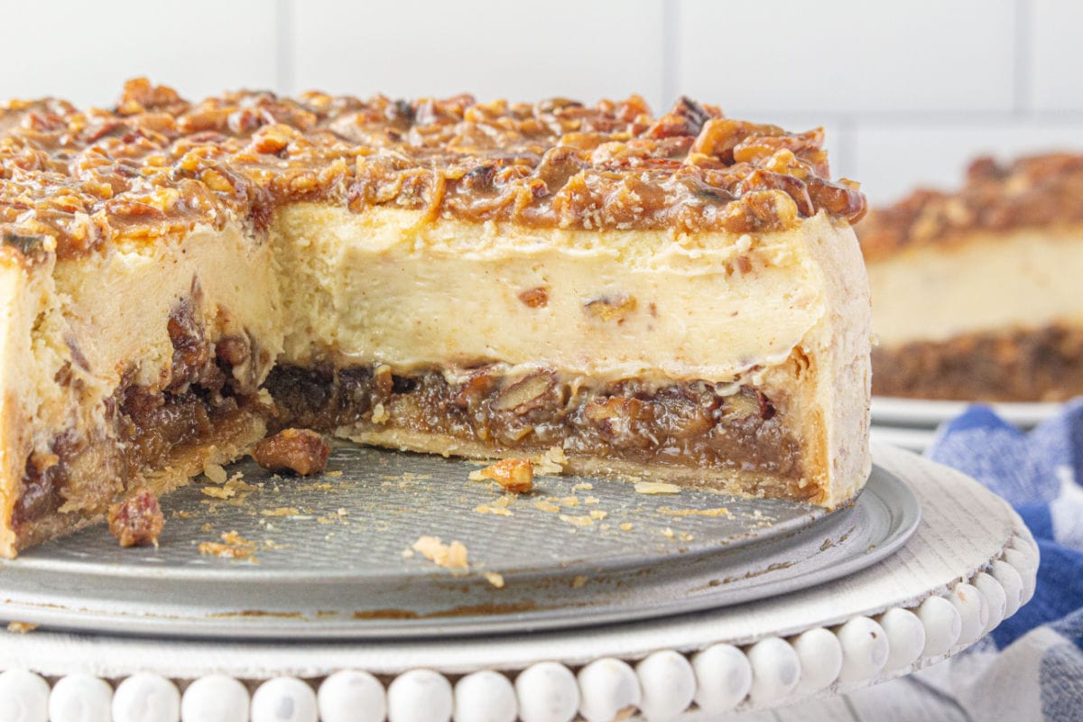 Cheesecake sliced open to show the layers of pecan pie, cheesecake, and topping.