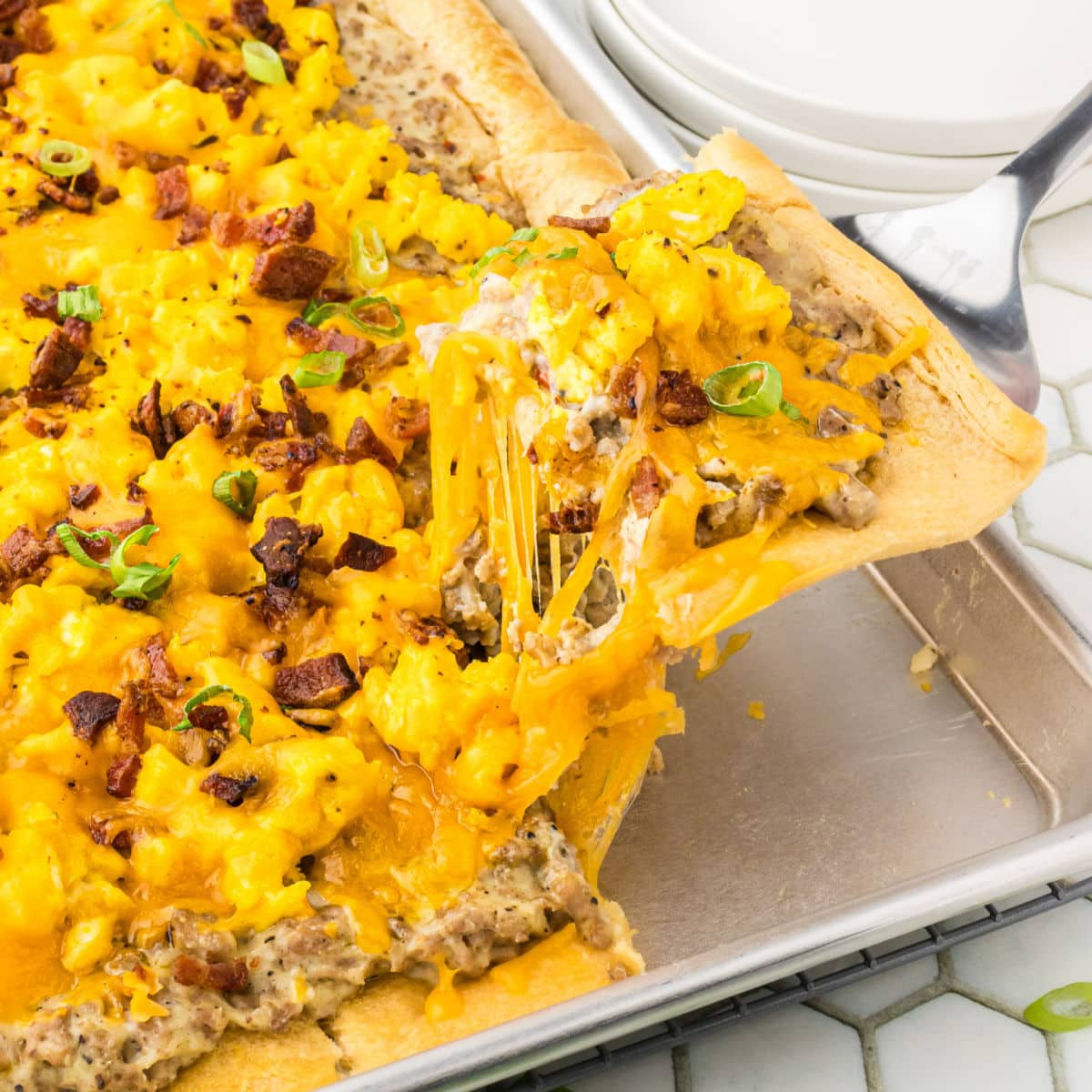 A serving of breakfast pizza being removed from the dish.