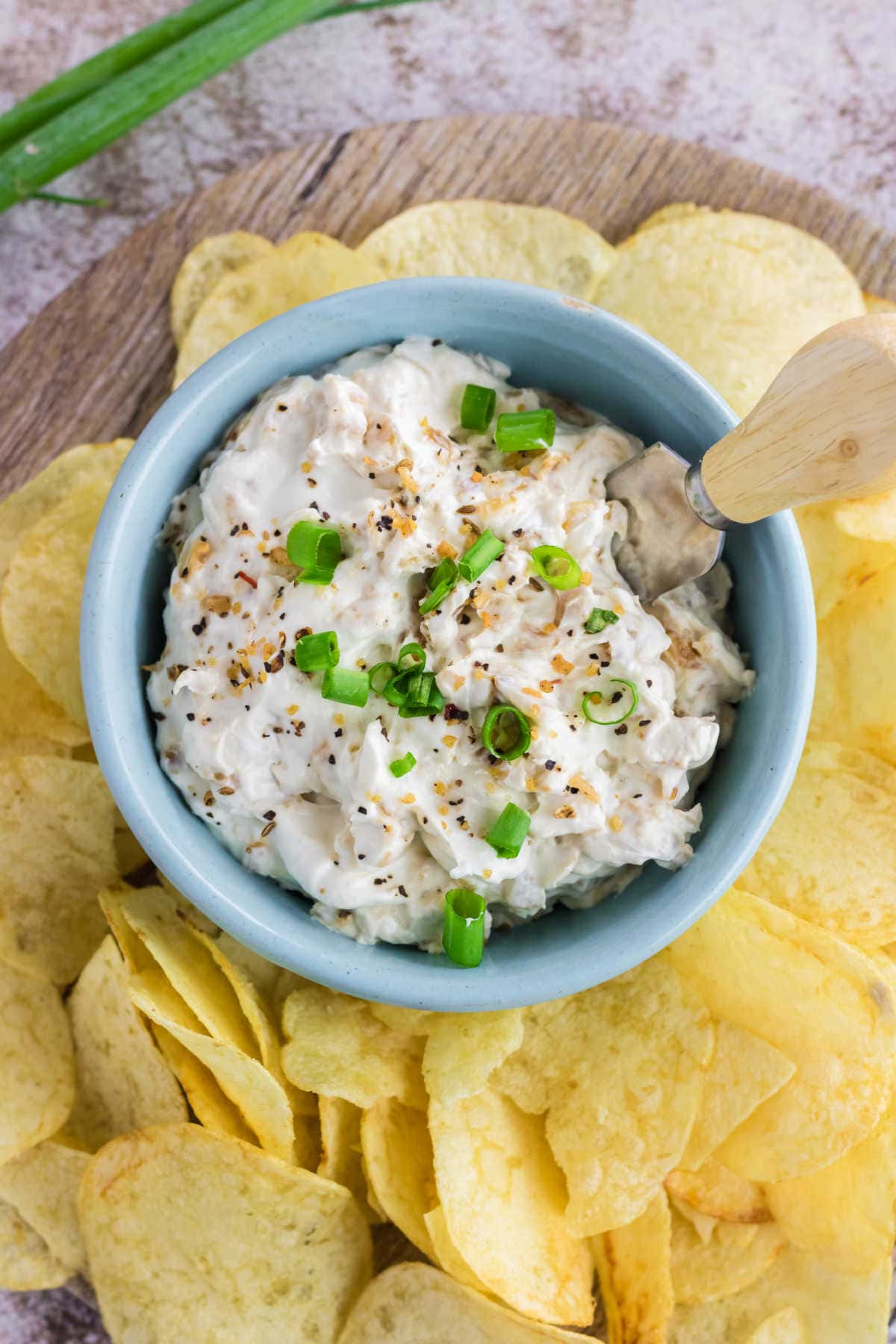 Overhead view of onion dip in a blue bowl garnished with green onions.