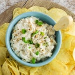 Overhead view of onion dip in a blue bowl surrounded by potato chips. A title text overlay for Pinterest is across the top.