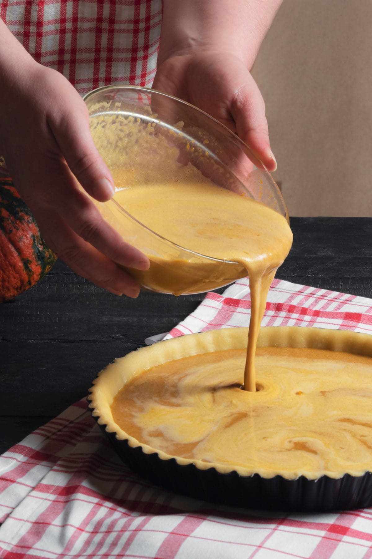 A woman's hands pouring pumpkin pie filling into a pie crust.
