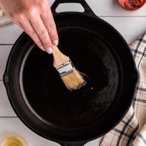 closeup of someone brushing a cast iron skillet with oil.