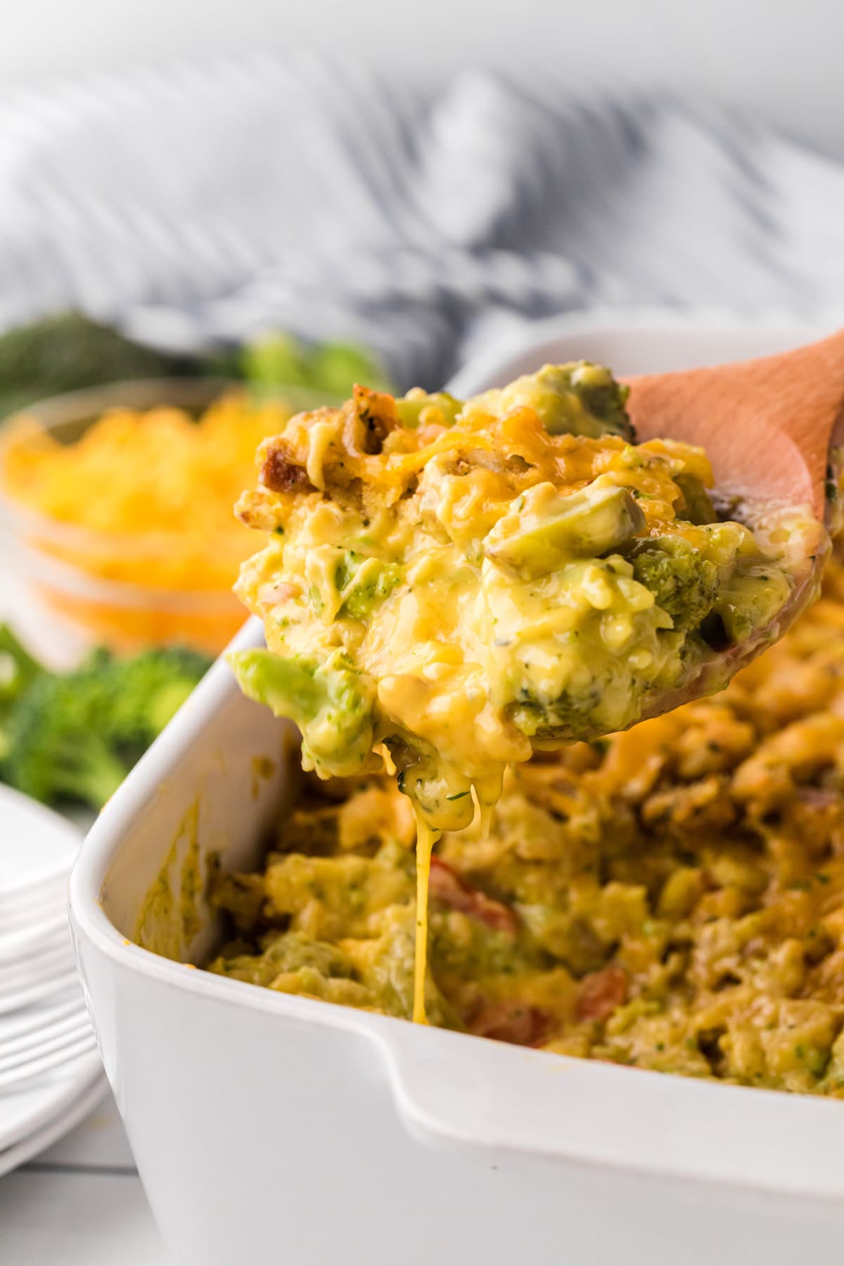 A wooden spoon scooping a portion of cheesy broccoli with stuffing out of a casserole dish.