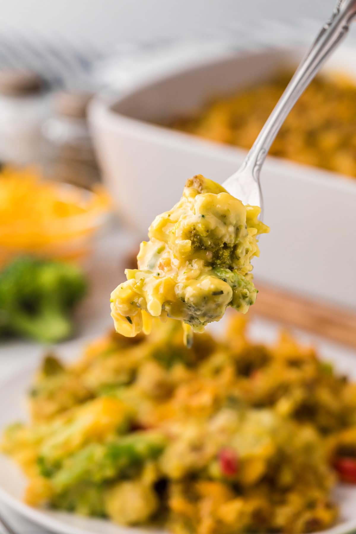 A fork holding a bite of broccoli and stuffing covered in melted cheddar cheese. 