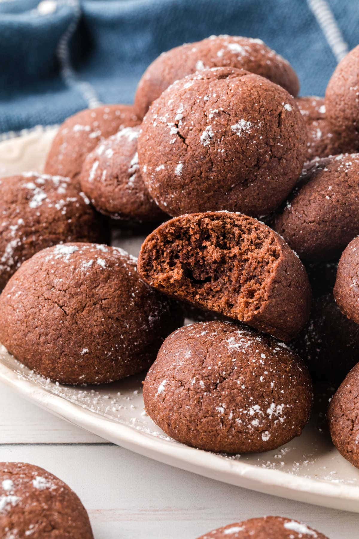 A plate full of chocolate butter cookies with one cut open to see the crumbly chocolate texture.