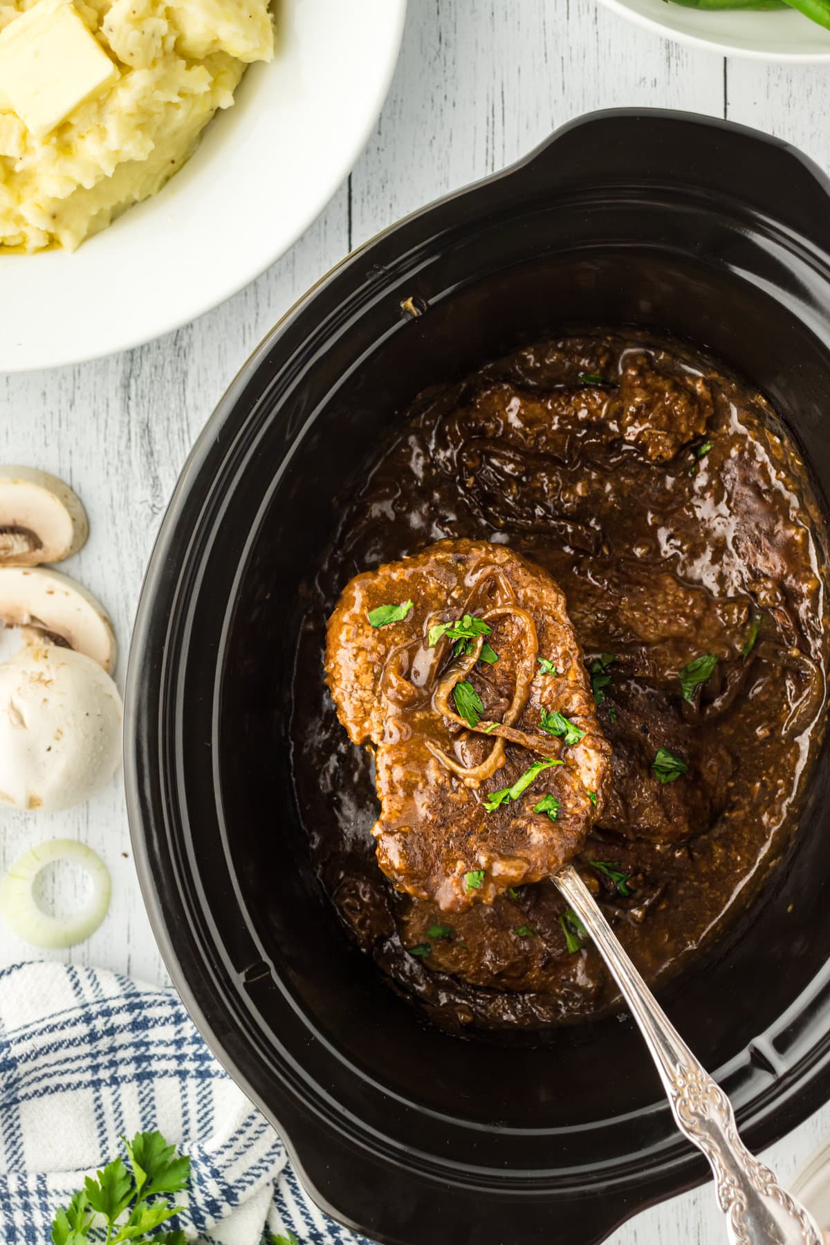 A finished cube steak covered with gravy being lifted from a slow cooker.