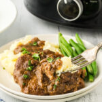 A plate of steak and gravy with mashed potatoes on a table.