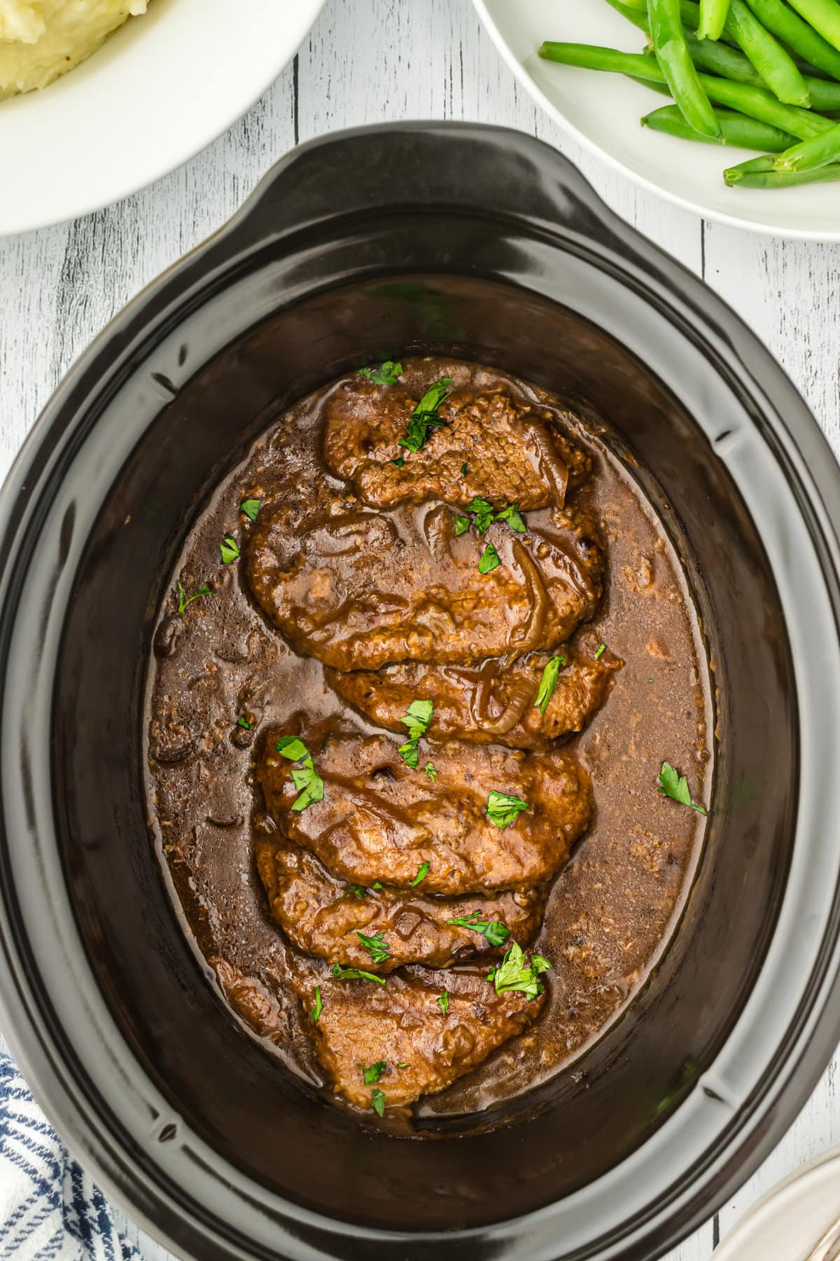 Overhead view of a slow cooker full of cube steaks and gravy.