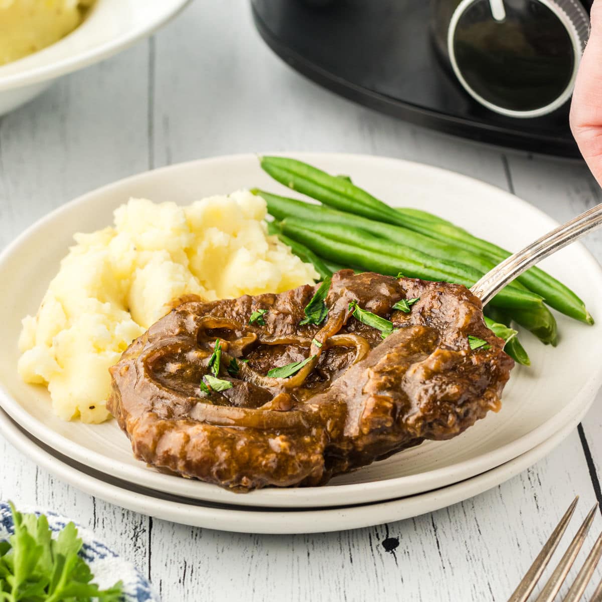 A cube steak covered with gravy on a white plate.