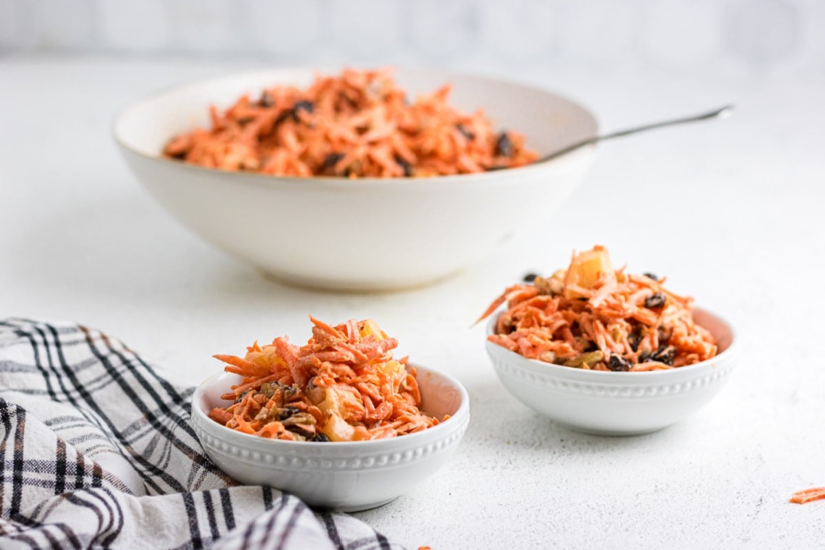 Carrot raisin salad being dished up into small serving bowls.