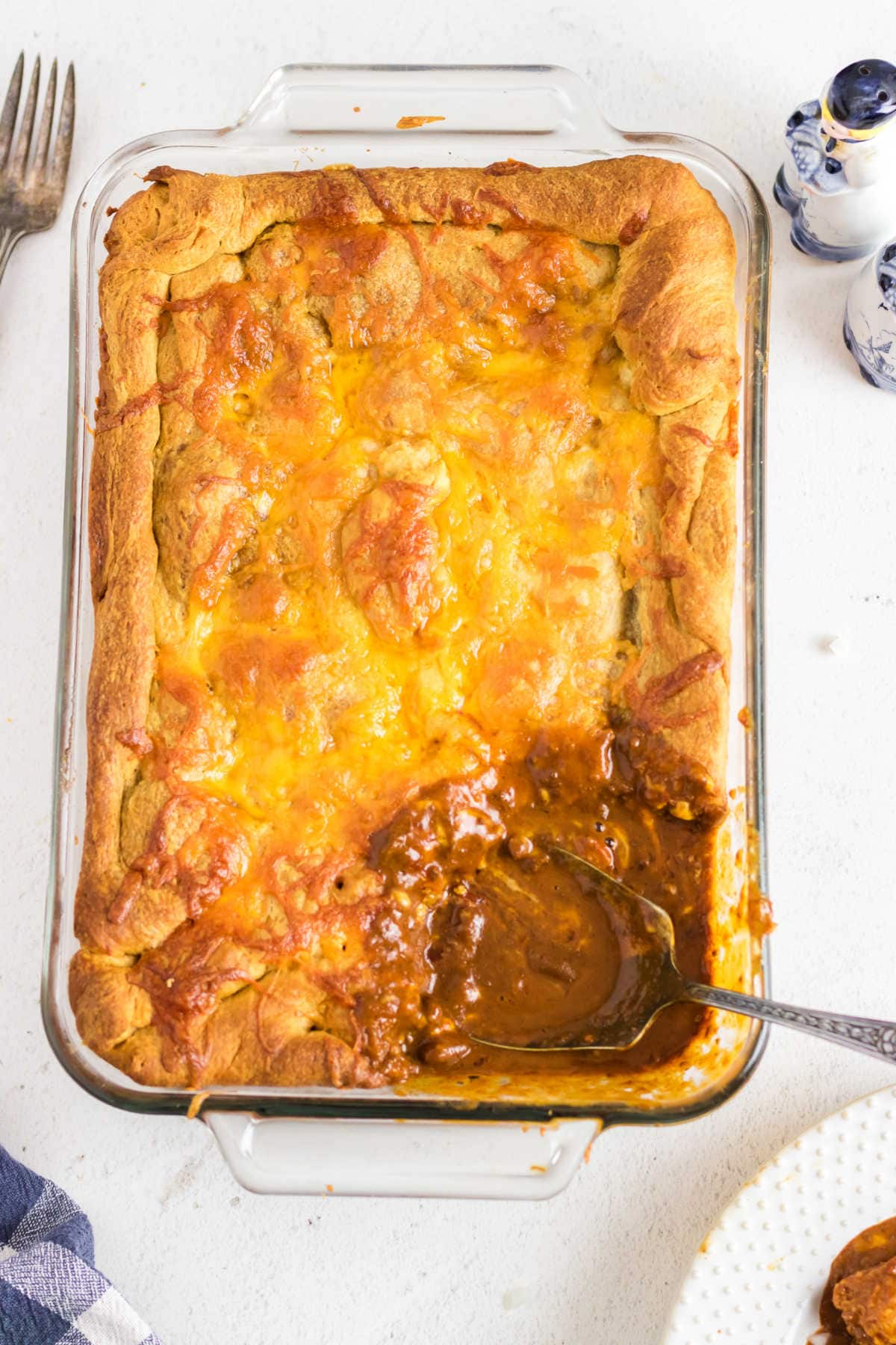 Casserole dish with a serving removed to show the chili dog filling and crispy, cheesy crust.