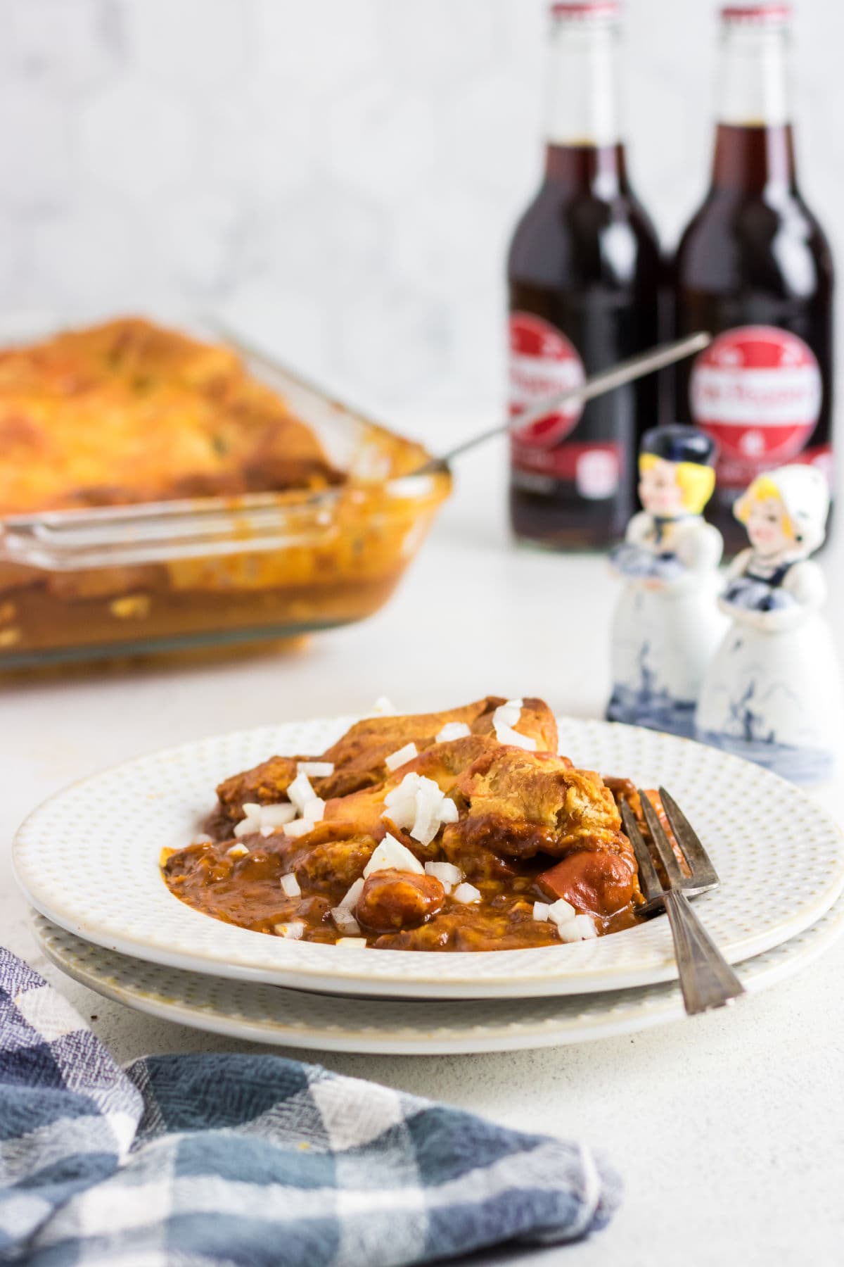 A table with a plate filled with casserole on it and Dr Pepper bottles in the background.