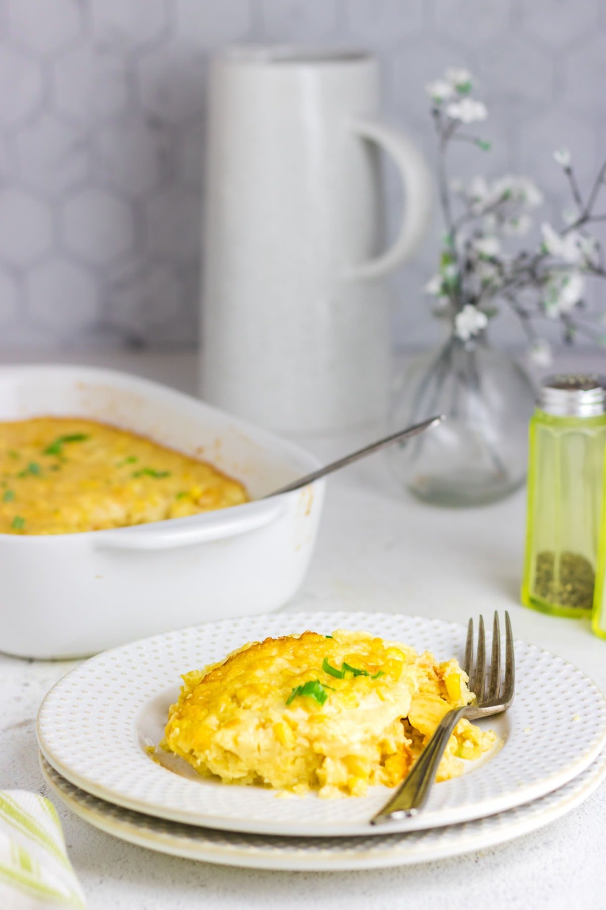 Corn pudding served up on a plate on a table that's been set for dinner.