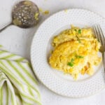 Overhead view of a plate of corn pudding on a table with a green and white linen.