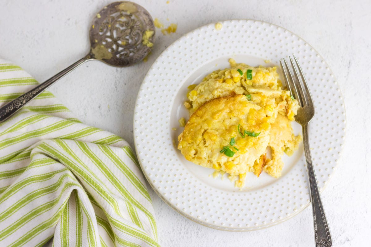 Overhead view of a plate of corn pudding on a table with a green and white linen.