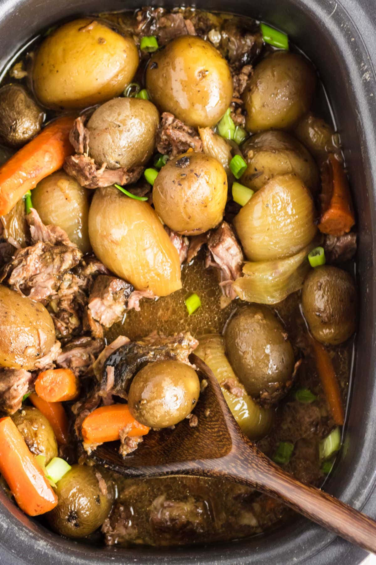 An overhead shot of a crockpot filled with beef stew, including baby potatoes, carrots, and pieces of beef.