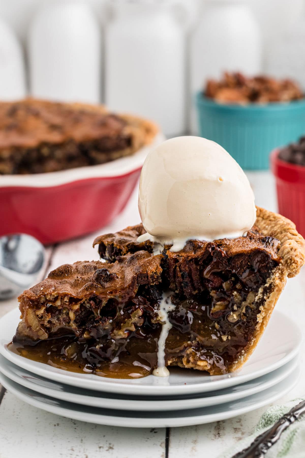 A slice of chocolate bourbon pecan pie on a plate with a shiny scoop of ice cream on top. The angle of the photo highlights the gooey, chocolate interior of the pie which runs a little onto the plate.