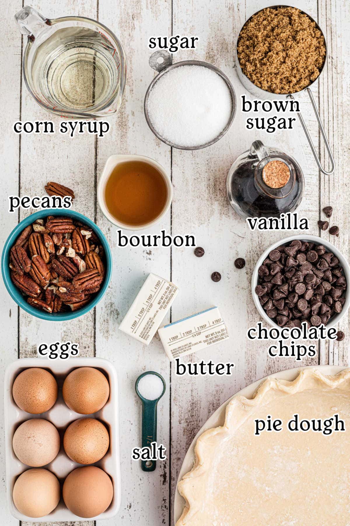 An overhead shot with text overlay of raw ingredients for chocolate bourbon pecan pie, including: corn syrup, sugar, vanilla, bourbon, pecans, eggs, chocolate chips, butter, and pie dough in various small bowls or measuring containers.