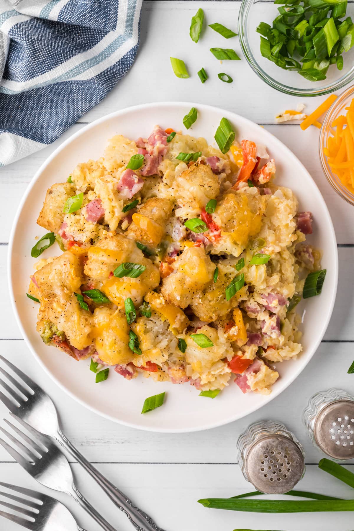 Cheesy tater tots, diced ham, chopped peppers, and sliced green onions on a white plate.