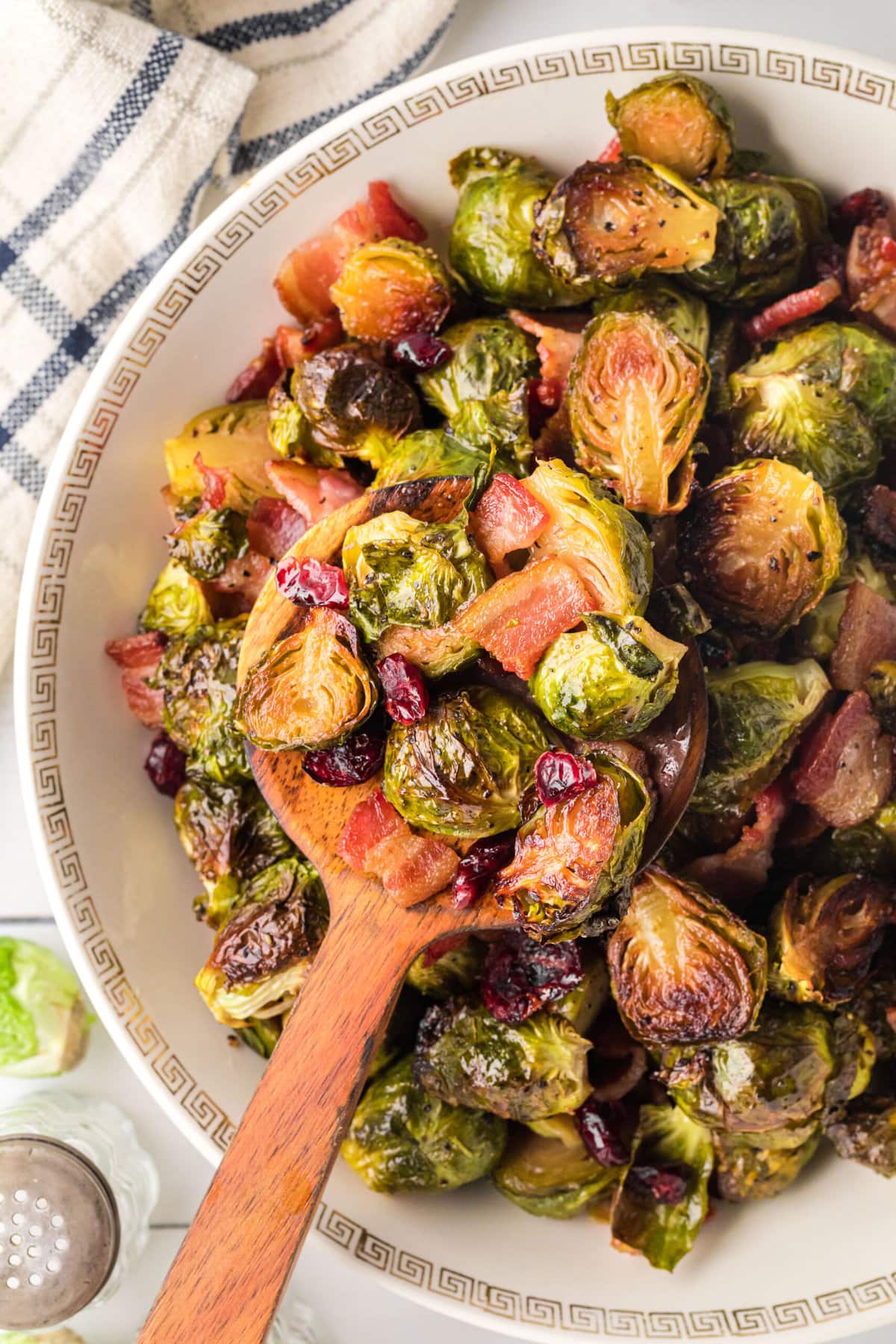 Roasted brussels sprouts with bacon and cranberries being spooned out of the serving bowl with a wooden spoon.
