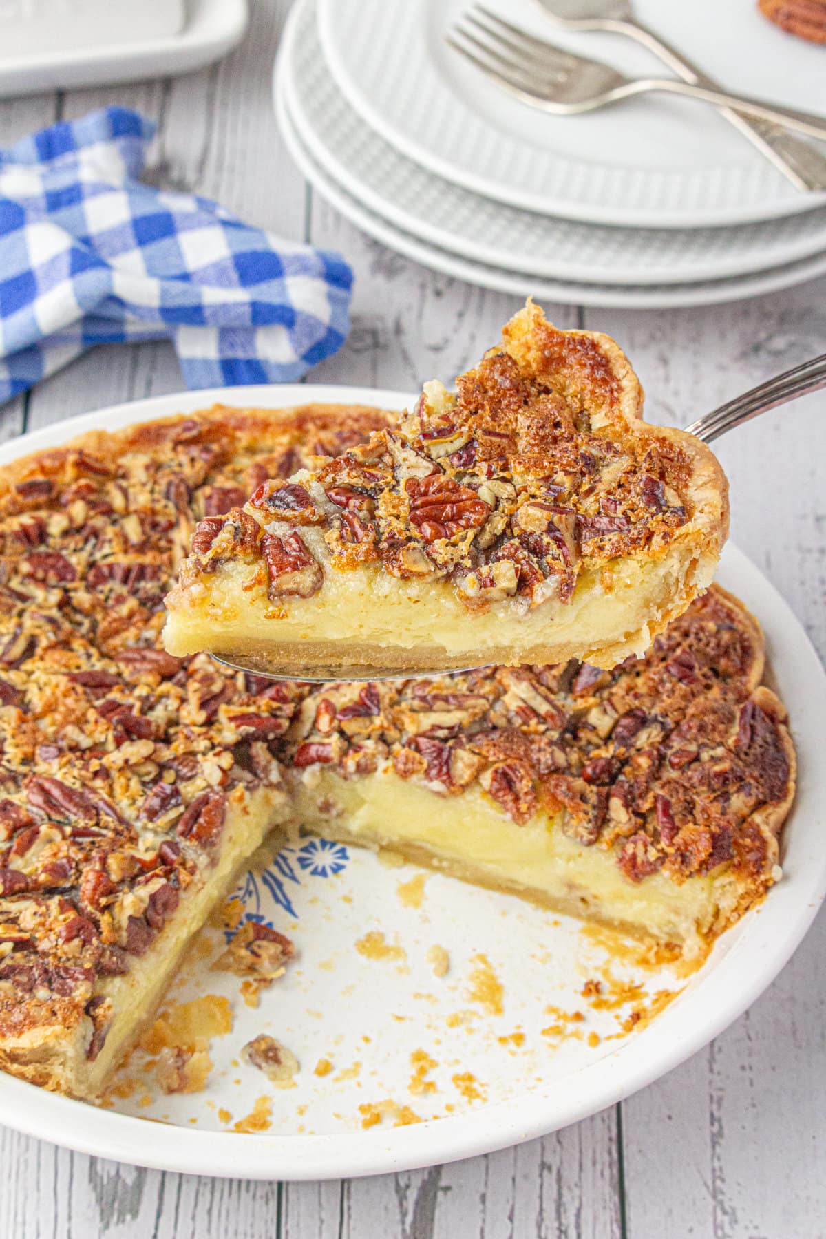 A slice of buttermilk pecan pie on a pie server hovering over the rest of the pie in a white ceramic dish.