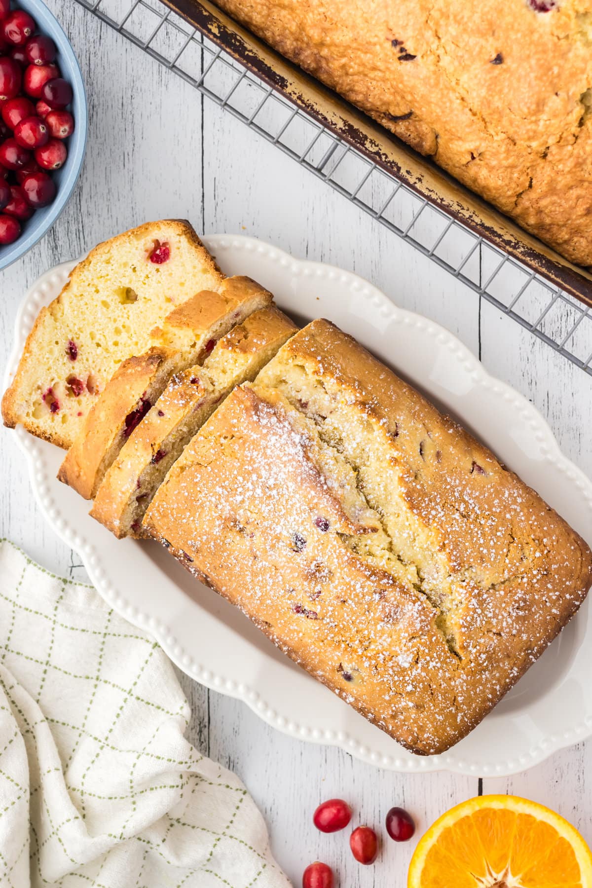 An overhead photo of the cranberry pound cake on a white platter. The cake is cut so cranberries are visible inside a few slices.