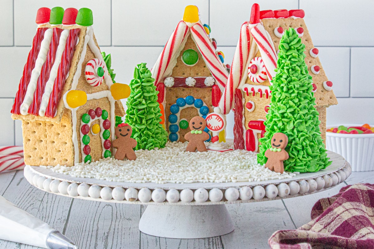 A trio of decorated gingerbread houses on a cake dish.