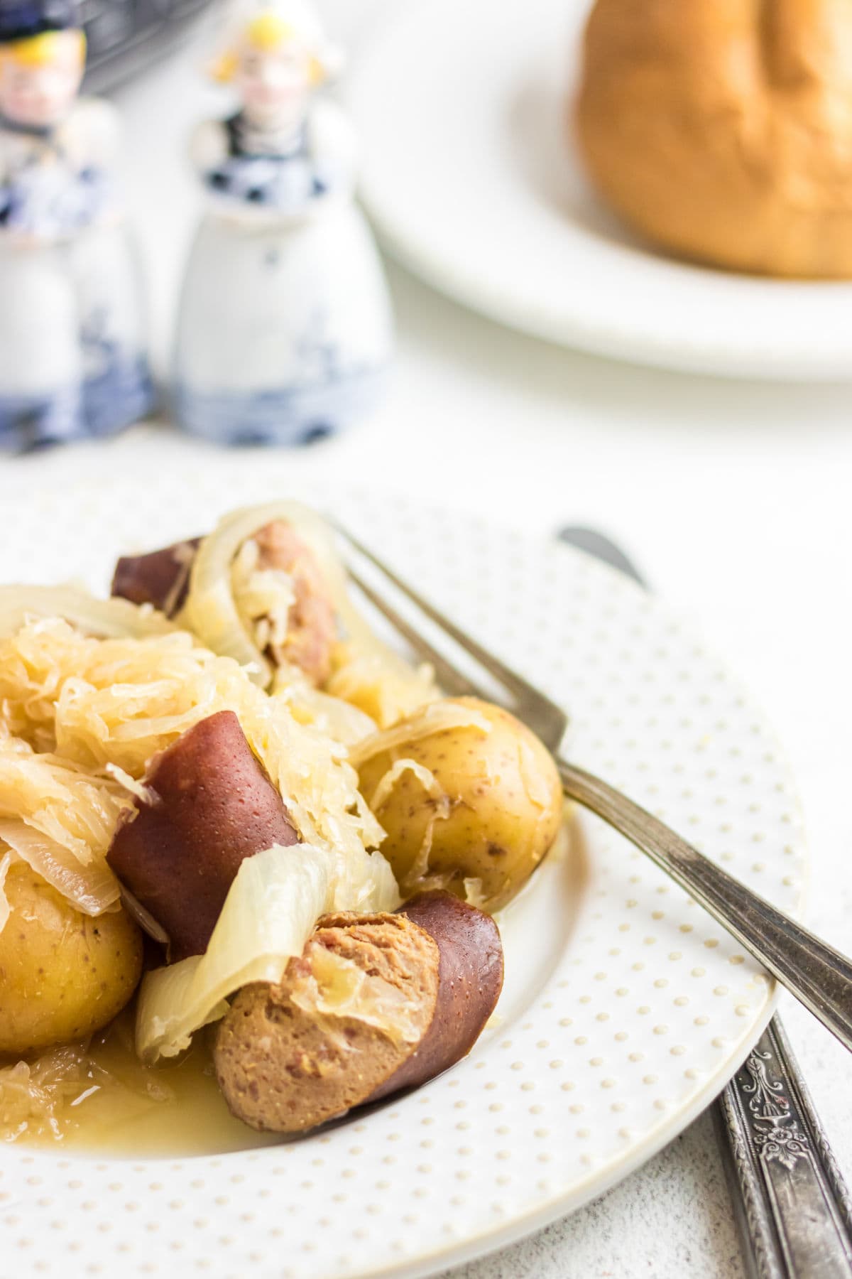 A close-up, angled photo of the meal on a white dish, highlighting the sliced kielbasa, potatoes, and sauerkraut. 