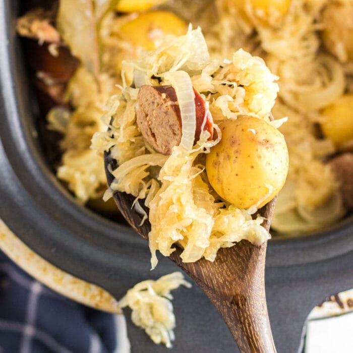 Kielbasa, potatoes, and sauerkraut being spooned out of a slow cooker.