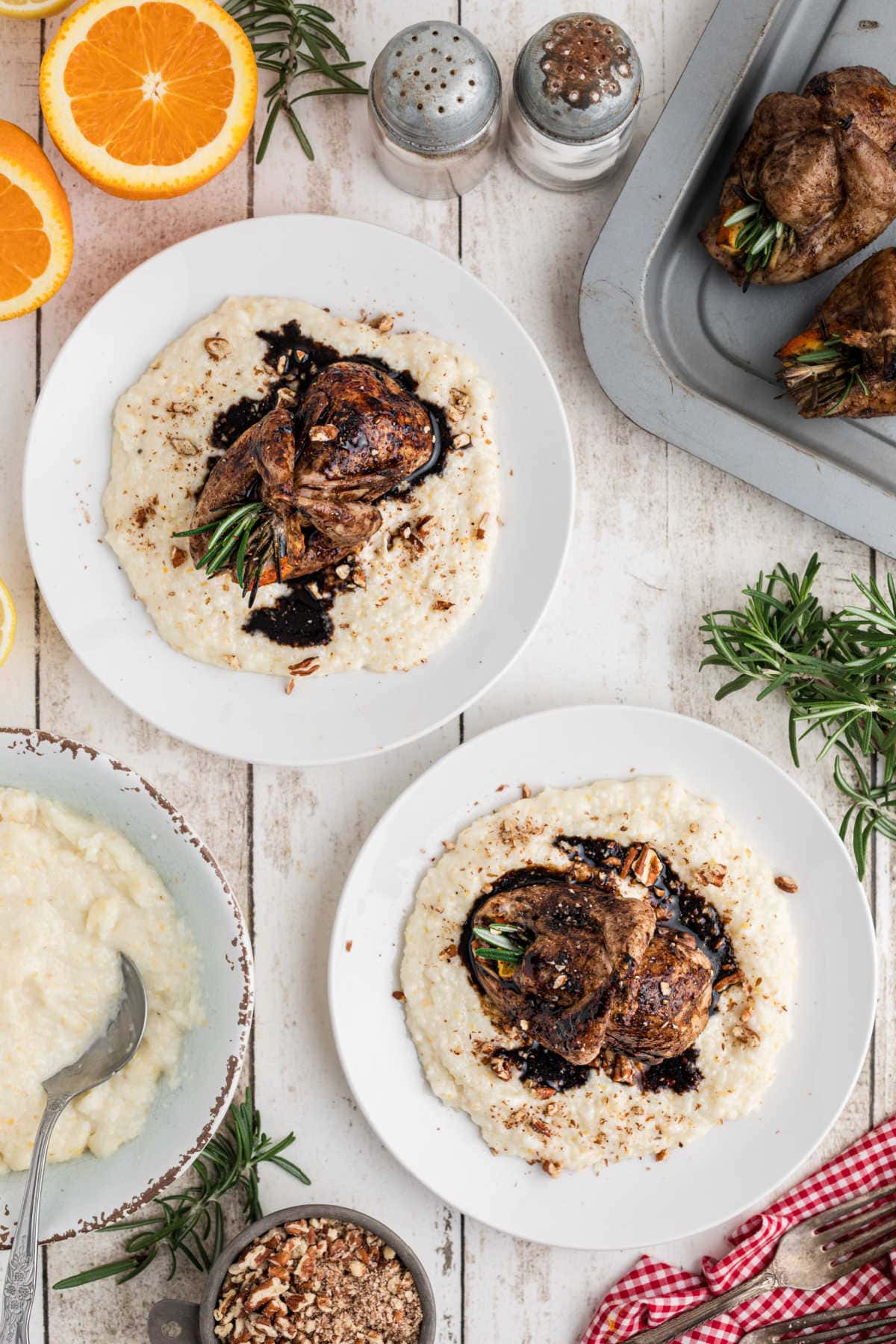 Two plates of roasted quail on cheese grits.