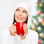 Woman dressed in white with a red coffee cup and a Christmas tree in the background. Title text overlay for Pinterest.