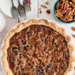 Overhead view of a chocolate bourbon pecan pie on the table. Text overlay for Pinterest.