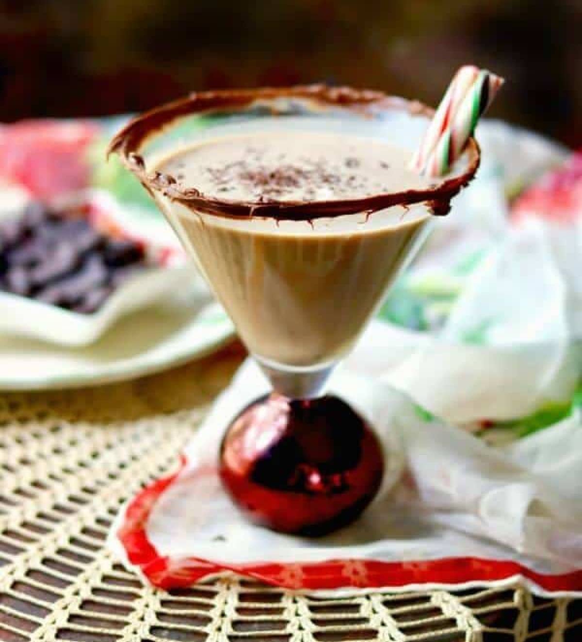 A chocolate cocktail in a martini glass with a chocolate rim and a peppermint stick.